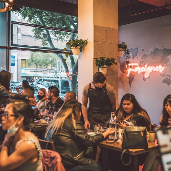 A bustling restaurant interior with patrons dining and a server attending to a table.