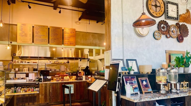 A rustic-industrial restaurant interior with a counter, menu boards, and decorative clocks on the wall.
