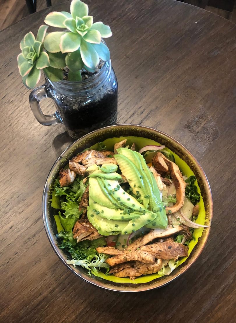 A vibrant salad with grilled chicken, avocado slices, and greens, next to a succulent plant.