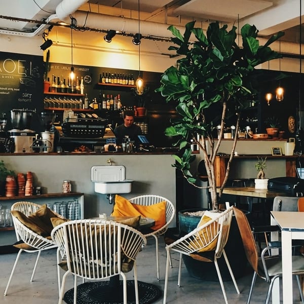 A cozy cafe interior with a barista behind the counter, customers, and modern seating.