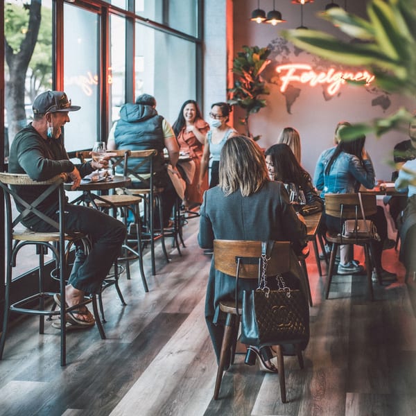 Lively restaurant interior with patrons enjoying drinks and a "Foreigner" neon sign.
