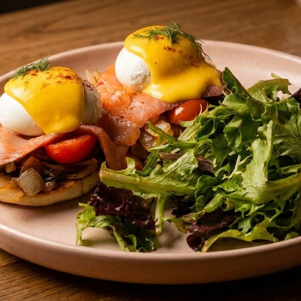 Eggs Benedict with smoked salmon, poached eggs, hollandaise sauce, and a side salad on a pink plate.