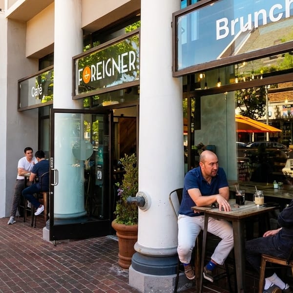 People dining outdoors at tables on a brick sidewalk in front of the "Foreigner Cafe".