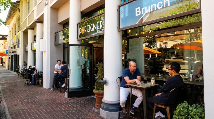 People dining outdoors at tables on a brick sidewalk in front of the "Foreigner Cafe".