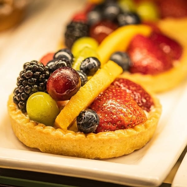 Close-up of a fruit tart with blackberries, grapes, blueberries, and strawberries on a white plate.