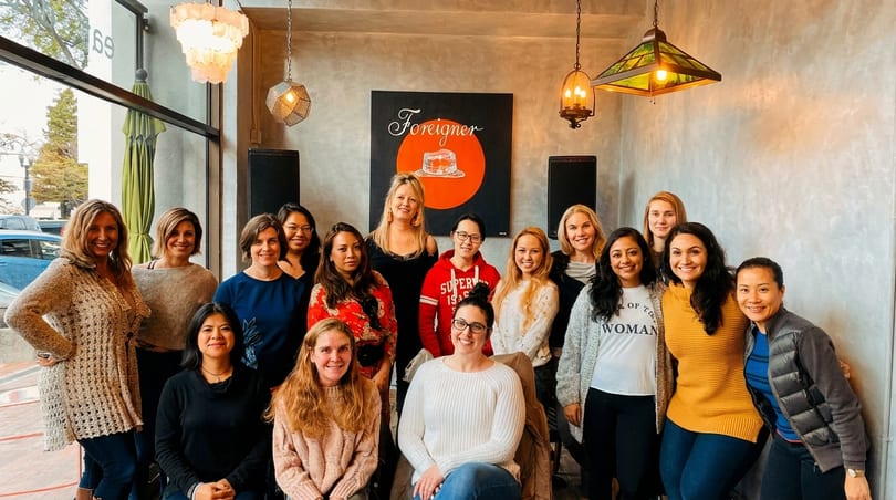 A diverse group of women smiling together inside a restaurant called Foreigner.